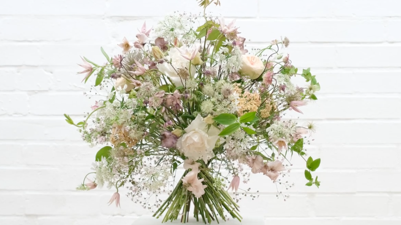 Open, airy hand-tied bouquet of garden roses, astrantia, achillea and clematis in blush and cream