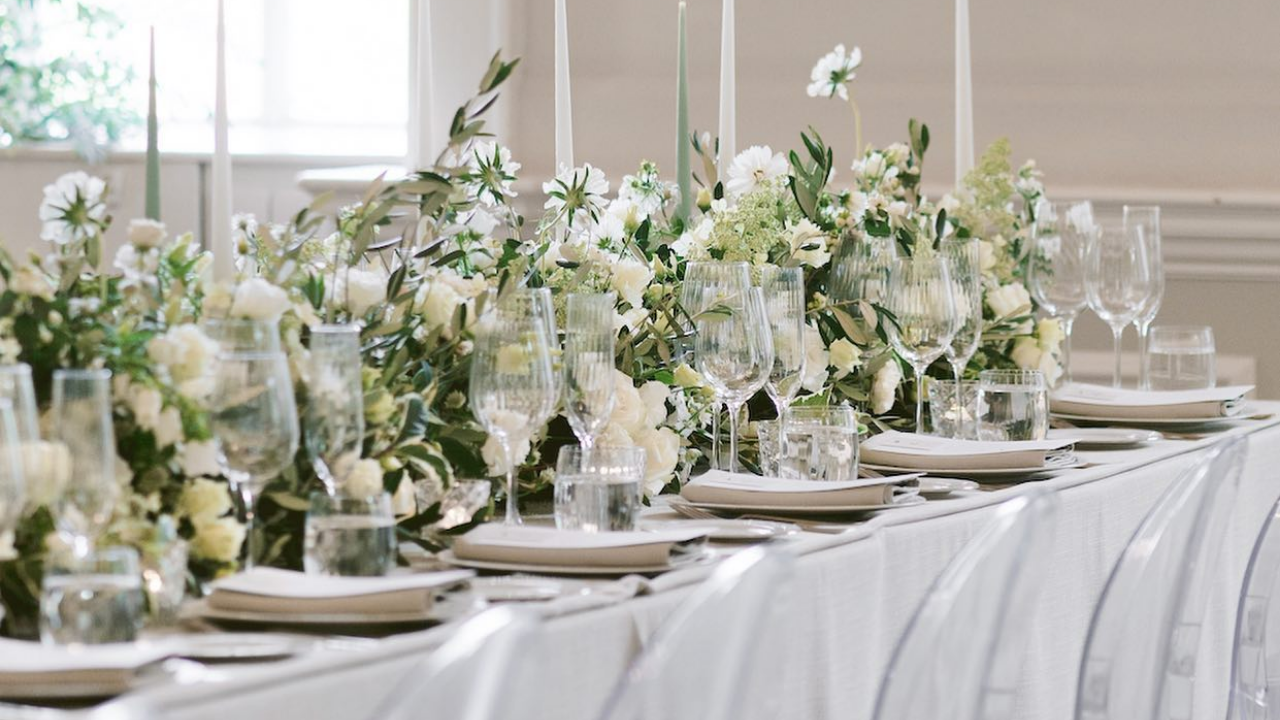A refined wedding reception table in Edinburgh, Scotland, styled with white and green flowers, olive foliage, tall tapered candles, elegant glassware and layered place settings.