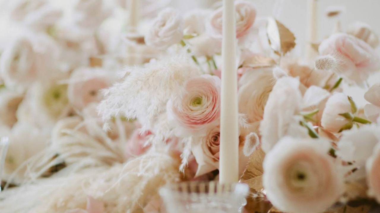 Romantic wedding tablescape featuring blush ranunculus, soft ivory florals, delicate dried textures and candlelight styling in an elegant editorial arrangement.