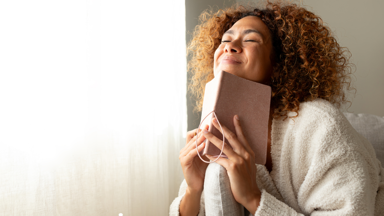 An african american woman is holding a journal with her eyes closed making a wish.