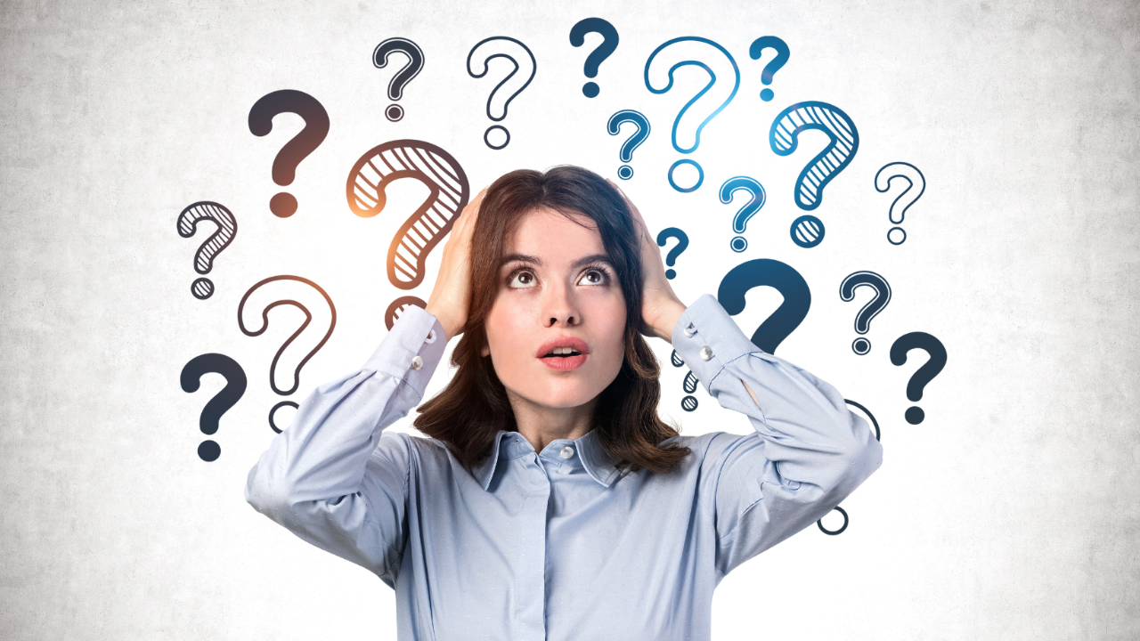 A dark-haired woman in a blue blouse holds her hands to her head and she's surrounded by colorful question marks as if she's confused.