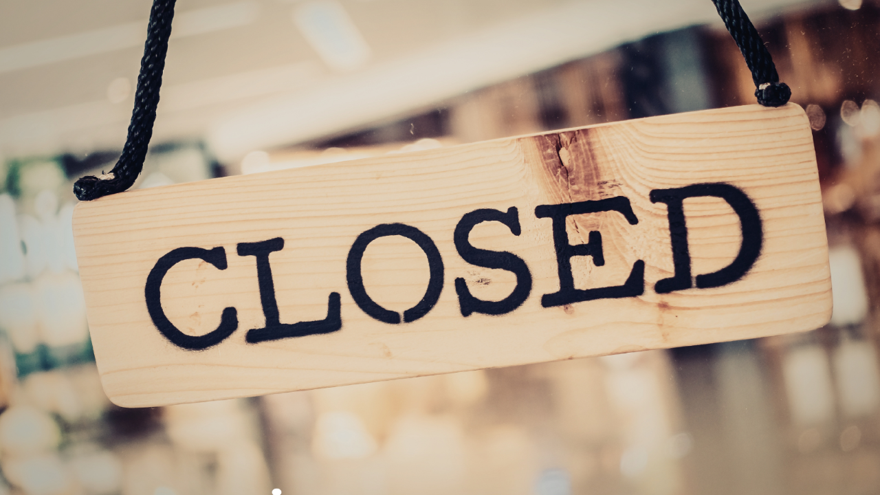 A wooden "closed" sign on the door of a brightly lit retail shop