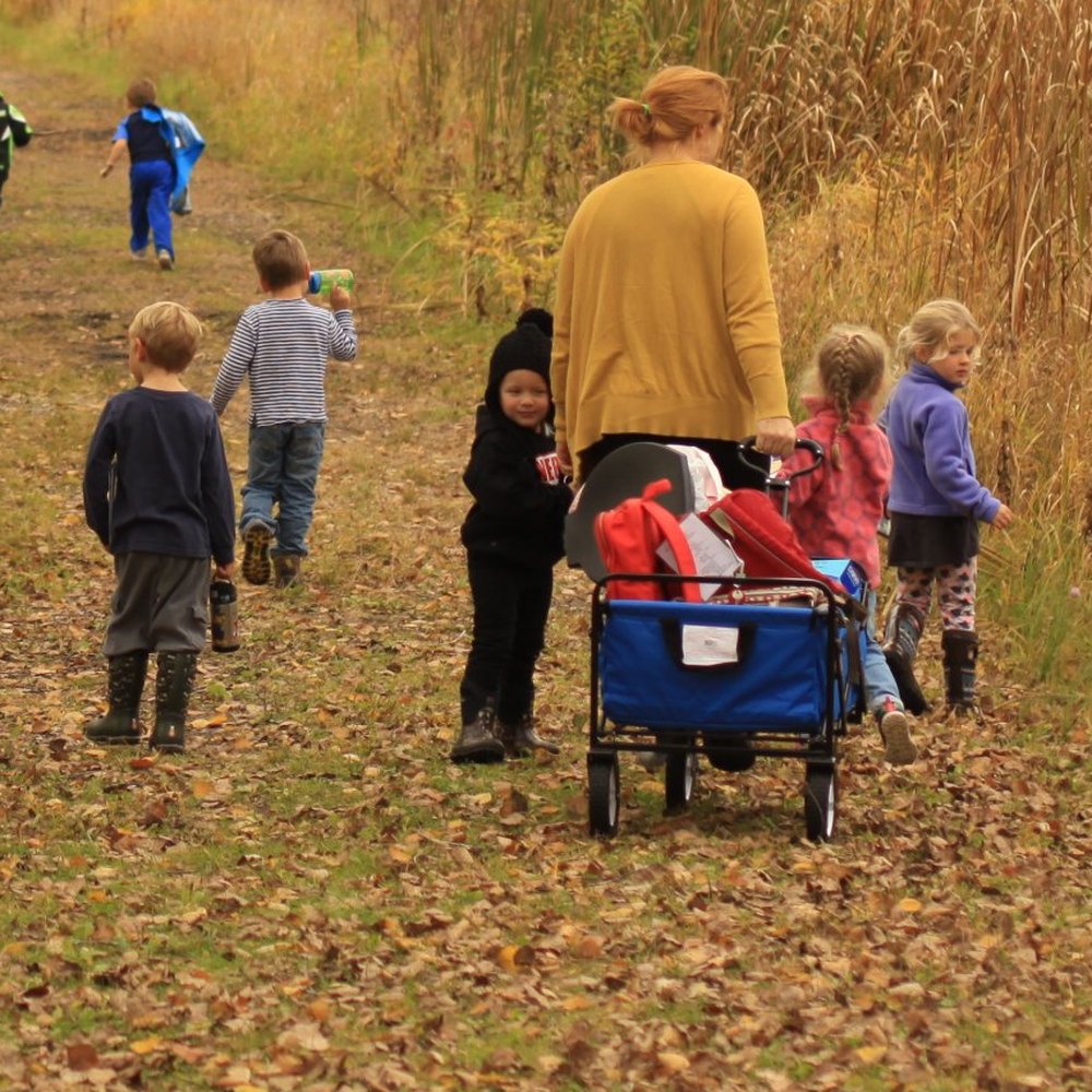 Kristen pulling a wagon down a fall forest trail with a group of preschoolers at Butterfly Hill