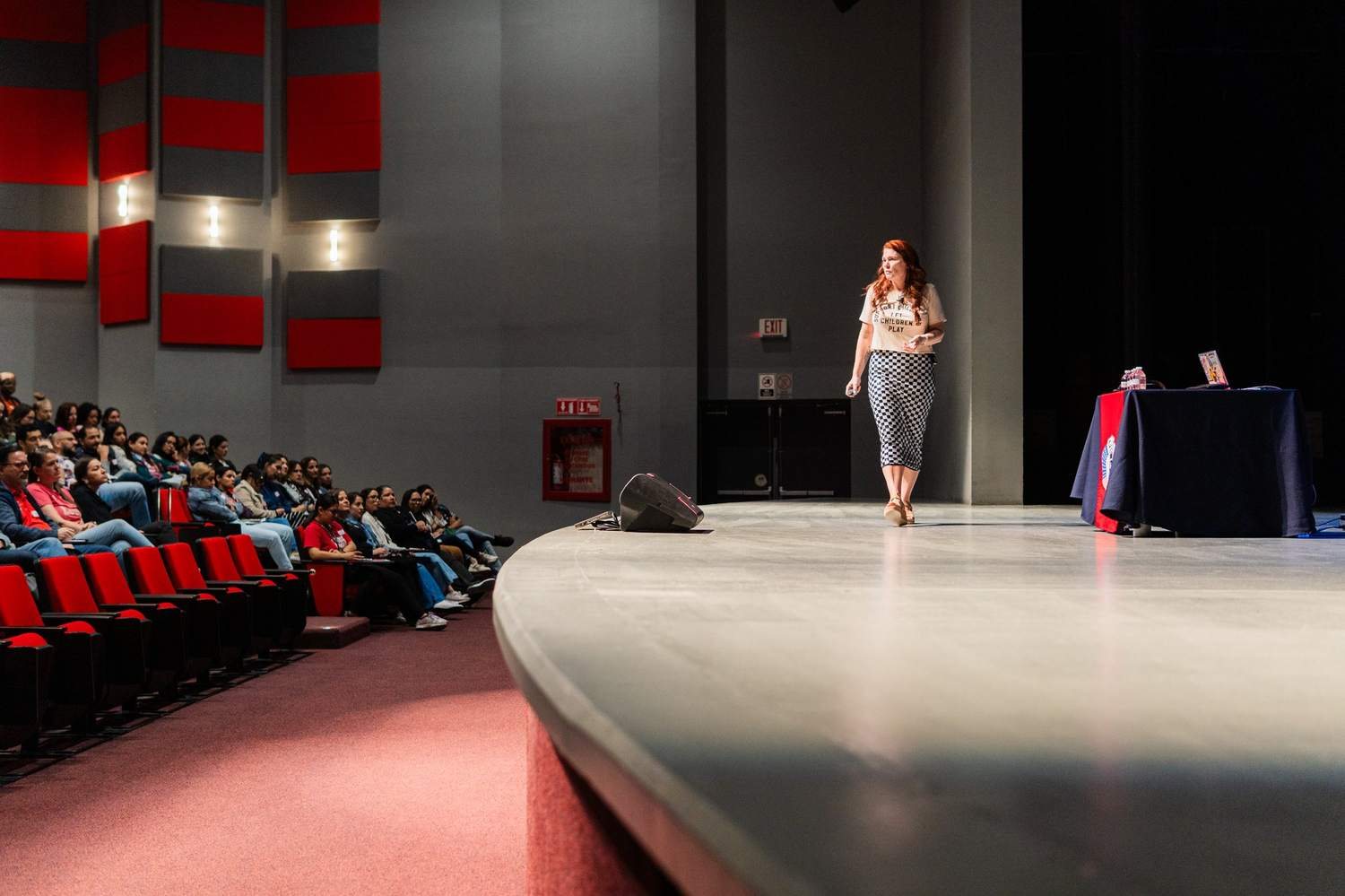Kristen walking a large auditorium stage in front of a seated audience