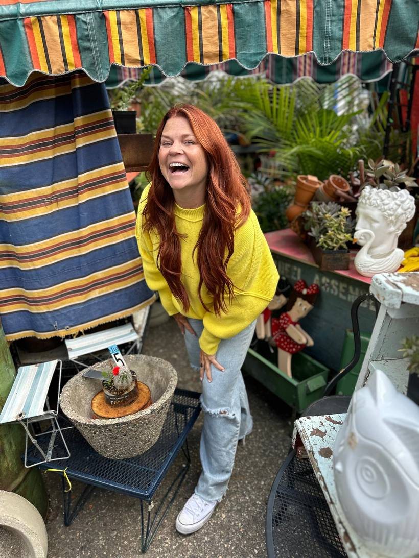 Kristen Day laughing in a yellow sweater at an outdoor flea market