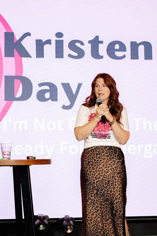 Kristen on stage holding a microphone in front of a large title slide