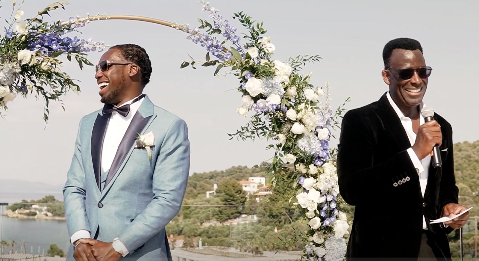 Terry J Lewis hosting a destination wedding ceremony with the groom under a floral arch overlooking the sea in Greece