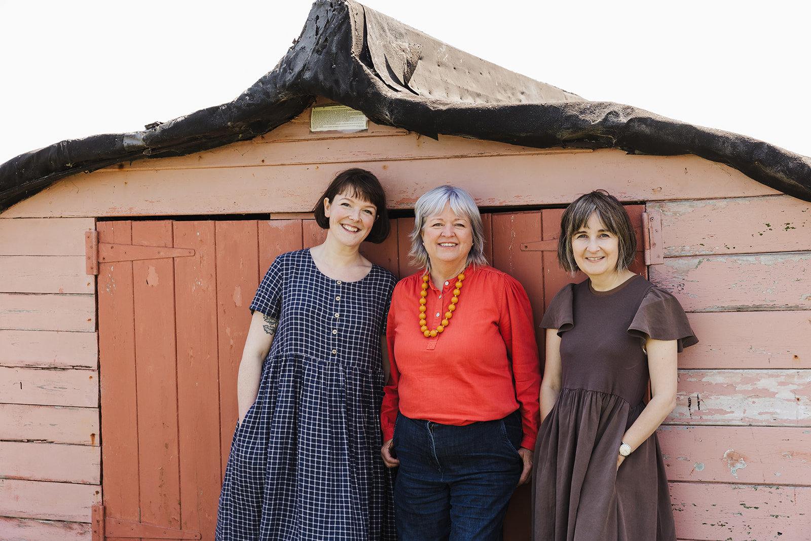 Tania, Katie and Helen standing smiling in front of an upturned boat, with 'the good ship illustration atlas' written above our heads.