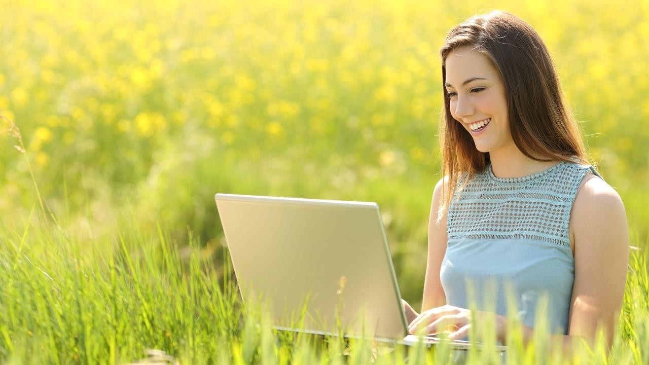 A woman in a meadow with a laptop, learning at her own pace