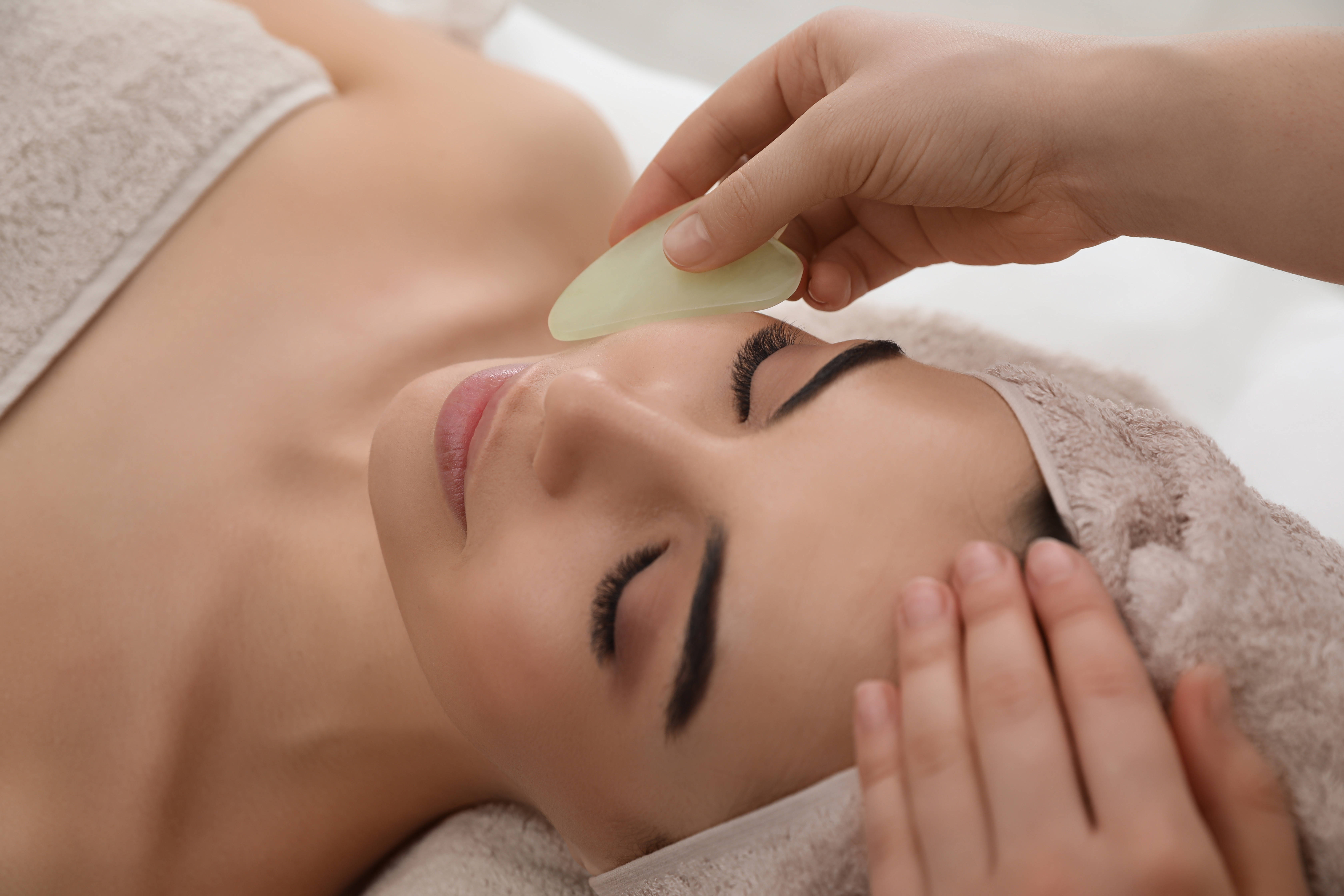 A therapist running a jade gua sha stone along the cheekbone during an EnerQi facial treatment