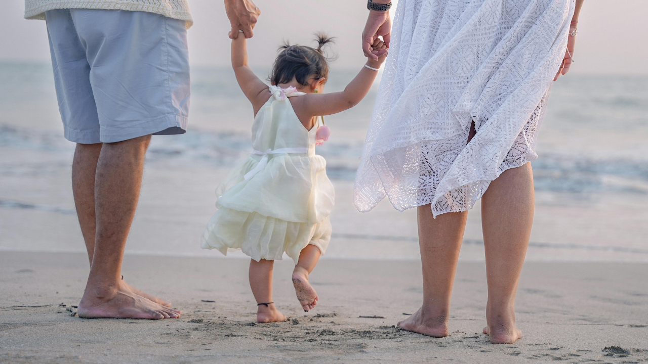 Child practising whole-foot steps in soft sand with parents to support toe walking development.