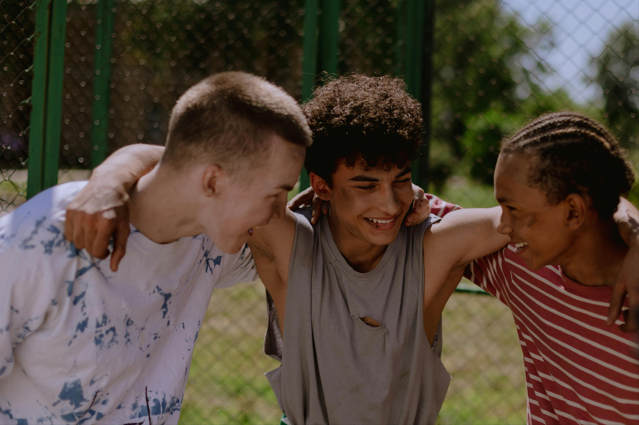 3 teenage boys smiling and hugging, showing they are happy and have a healthy friendship 