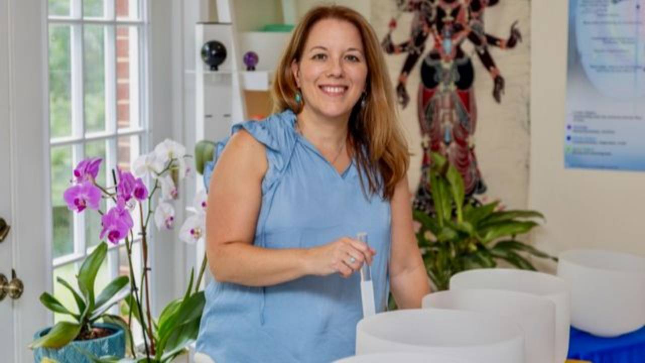 Red headed woman with a white tank top holding a white crystal singing bowl