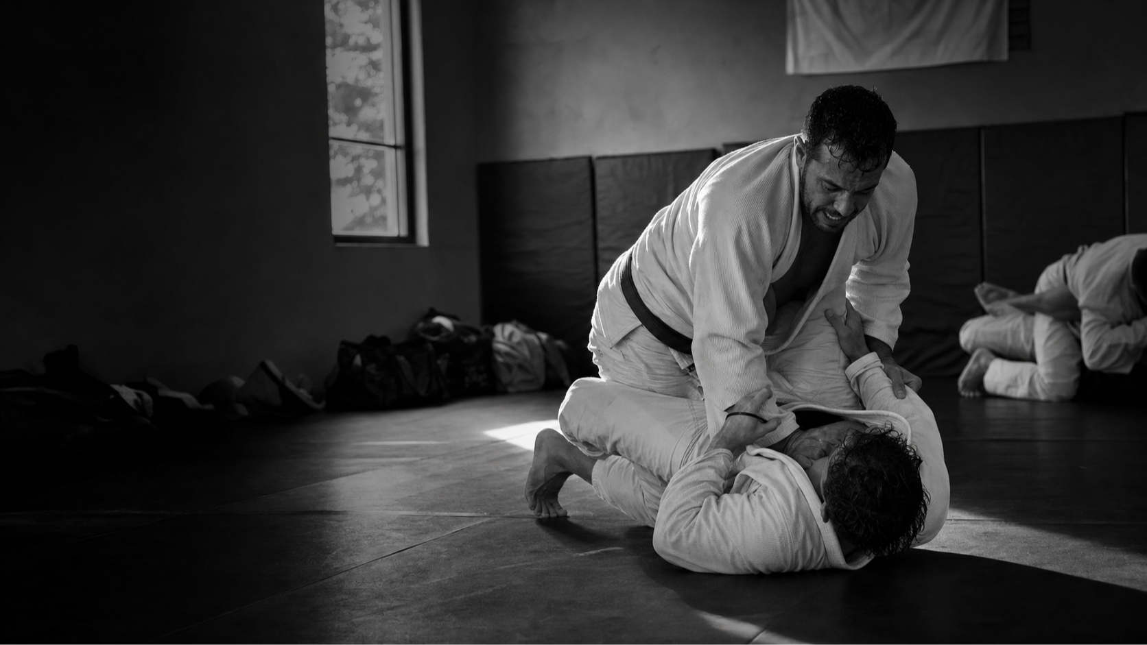 Coach guiding a grappler through a live training round — black-and-white academy photo