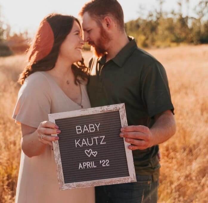 A fertility nutrition coaching client stands with a sign announcing a baby