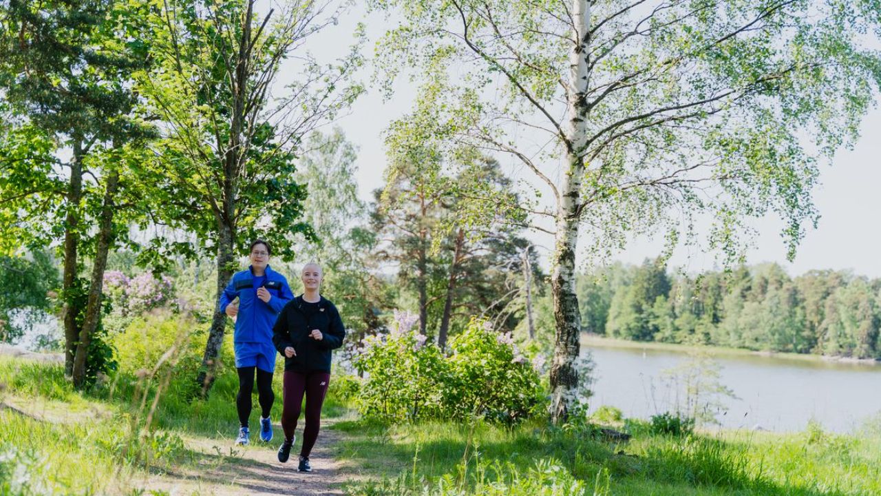 Kaksi juoksijaa metsäpolulla järven rannalla