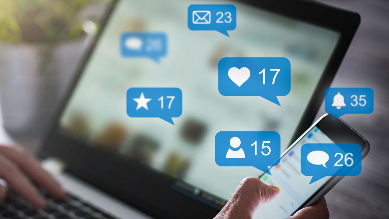 Personon lap top and phone with like icons coming out of the laptop