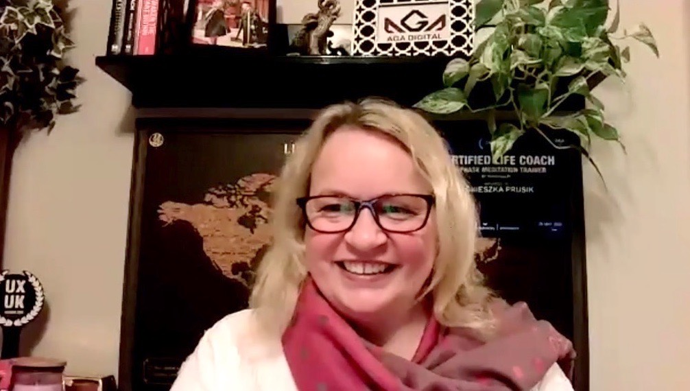 Coach Aga at home, smiling, wearing glasses, in the background is her home office