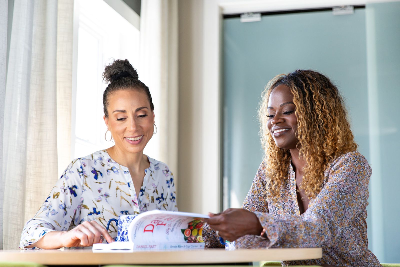 two women sitting at table looking at book