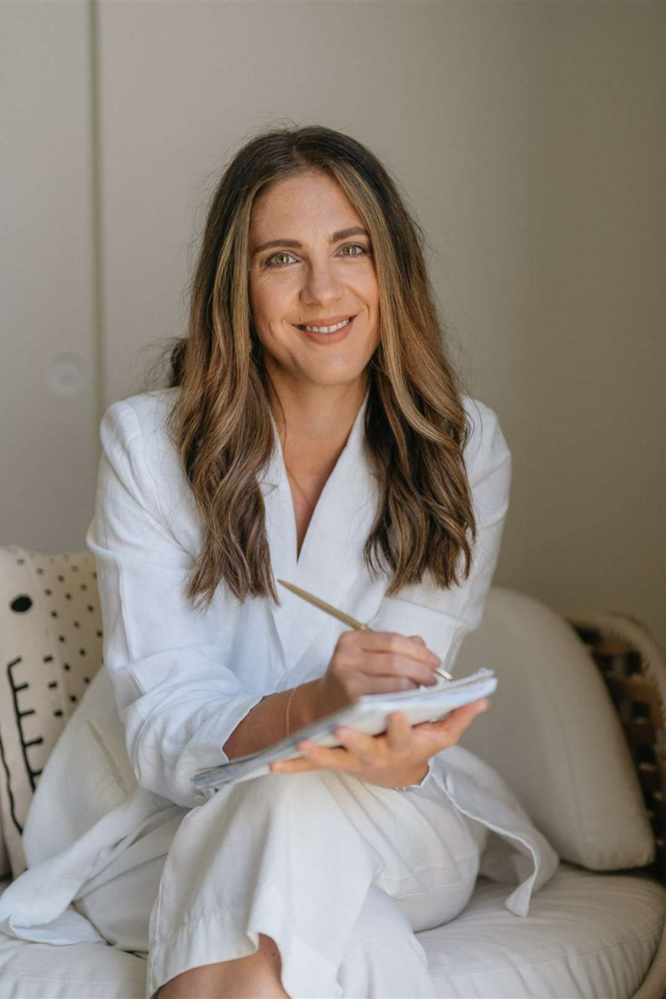 Hareta sitting on couch holding a cup of tea with crossed legs smiling at camera