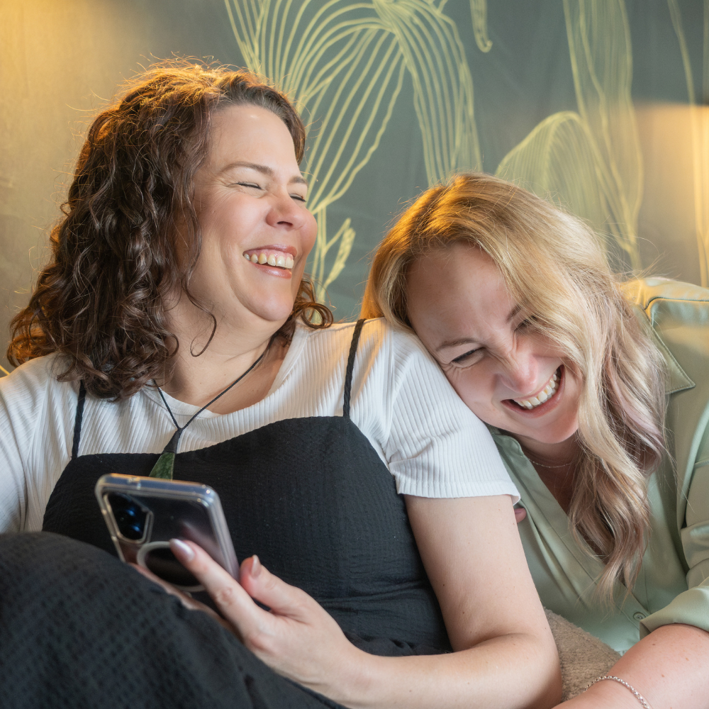 Sam and Jo, virtual assistant coaches, sitting on park bench laughing