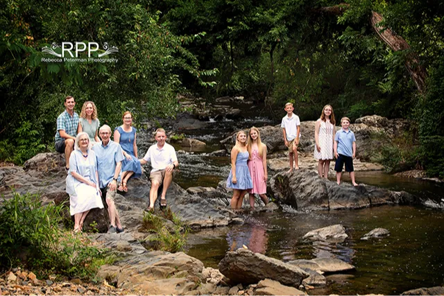 Extended family wearing blue pink beige posed on rock bridge in woods