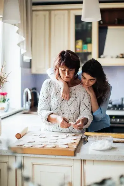 Mother and adult daughter standing in kitchen making cookies