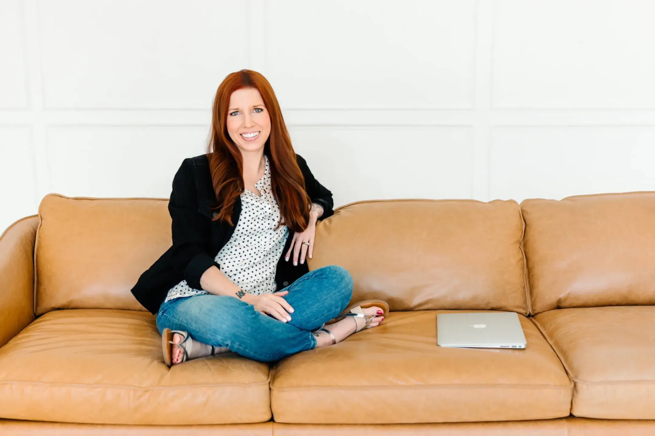 Carrie Howard sitting cross legged on a leather couch smiling