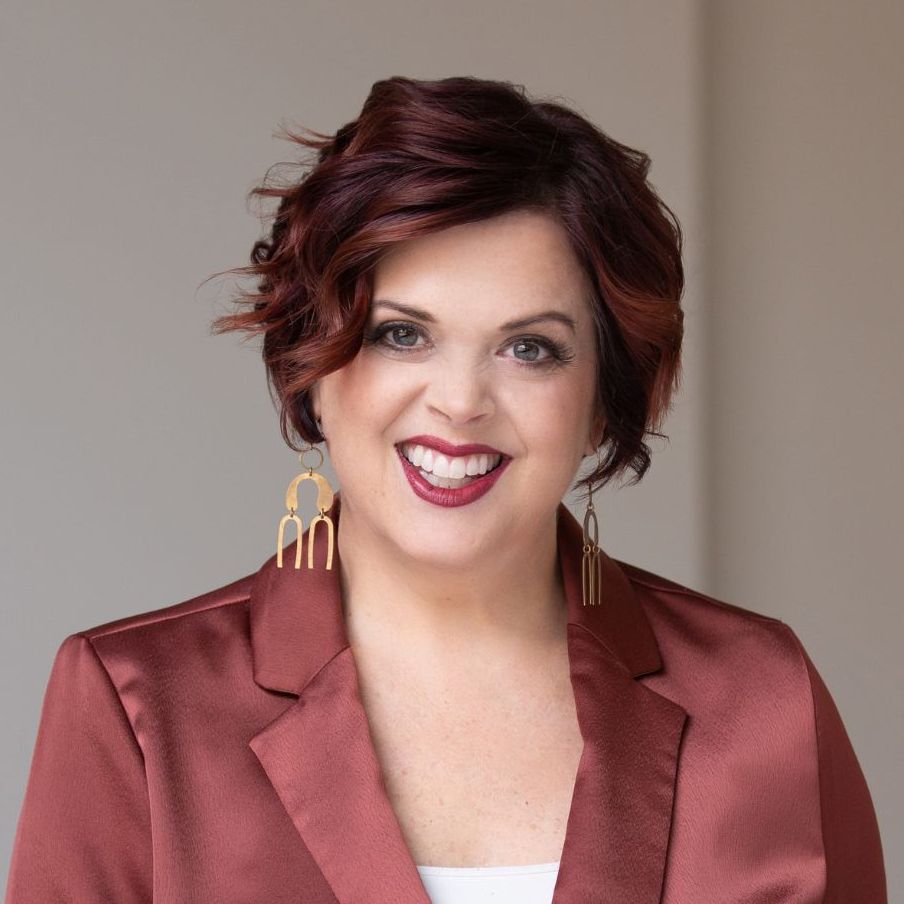 Dr Erika Salina against a dark background, finger to her forehead in a 'thinking' gesture