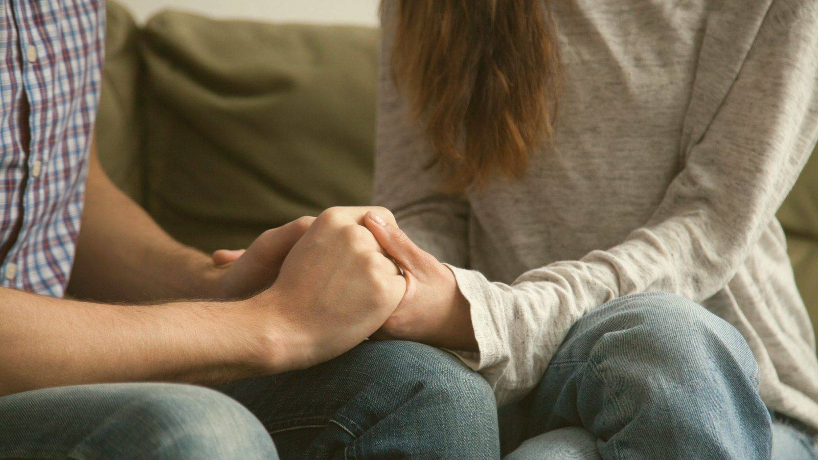 A couple sitting together on a sofa, hands clasped, working through a relationship pattern