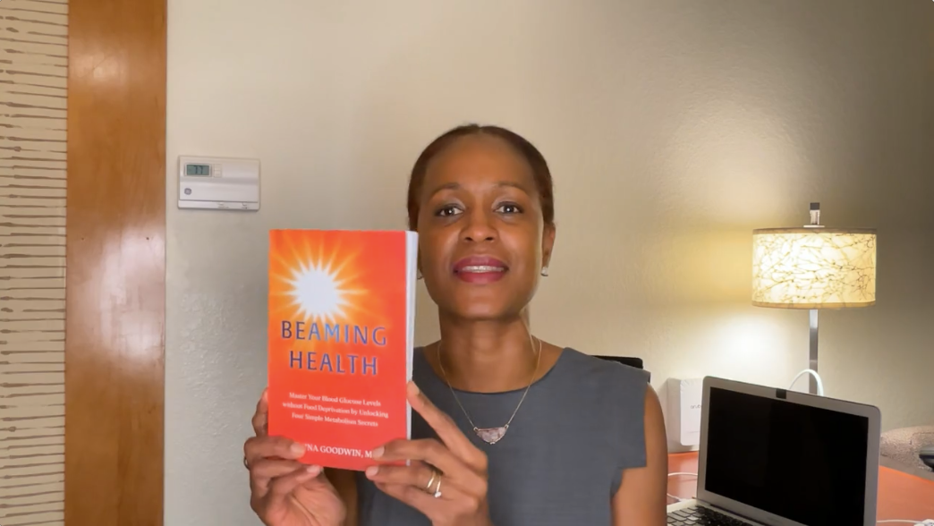 Dr. Amina Goodwin MD holding her book Beaming Health, a guide to metabolic health and blood sugar control