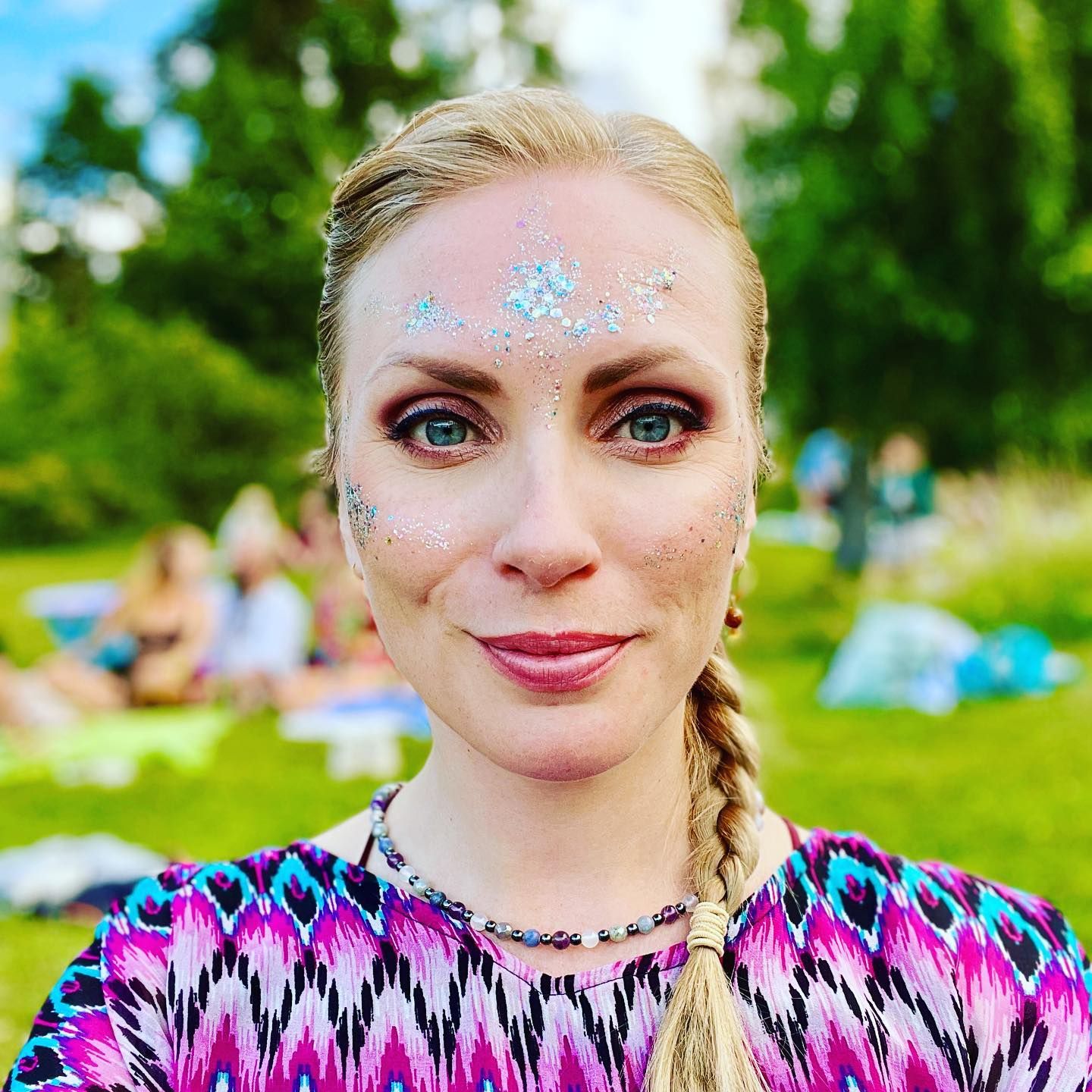 Grethe wears bright sparkly makeup in a green summer park.