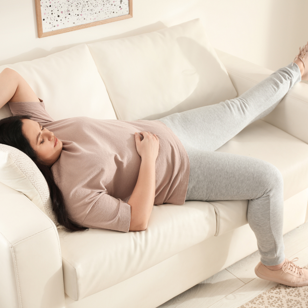 A young woman resting on a couch, arms wrapped around her torso