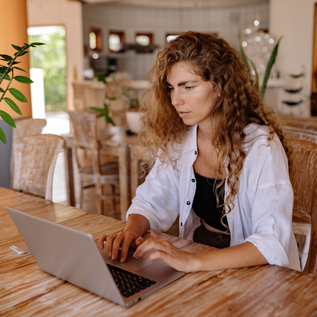 A smiling young woman sitting on her bed looking at a laptop screen