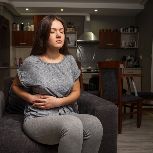 Woman in a dressing gown holding her lower abdomen in pain