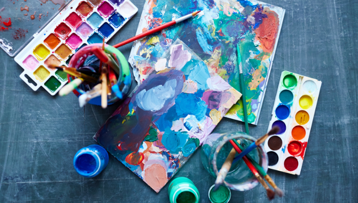 2 palettes, brushes, jars of water and abstract paintings on a table 