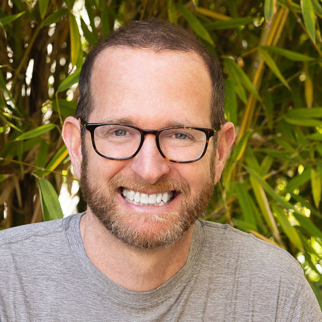 Jivana Heyman wearing brown glasses and a gray shirt.