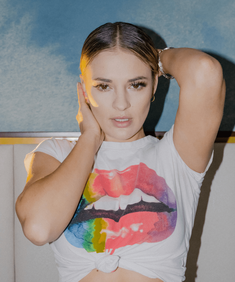 Woman posing with hands on head wearing a white t-shirt with a rainbow lip on it