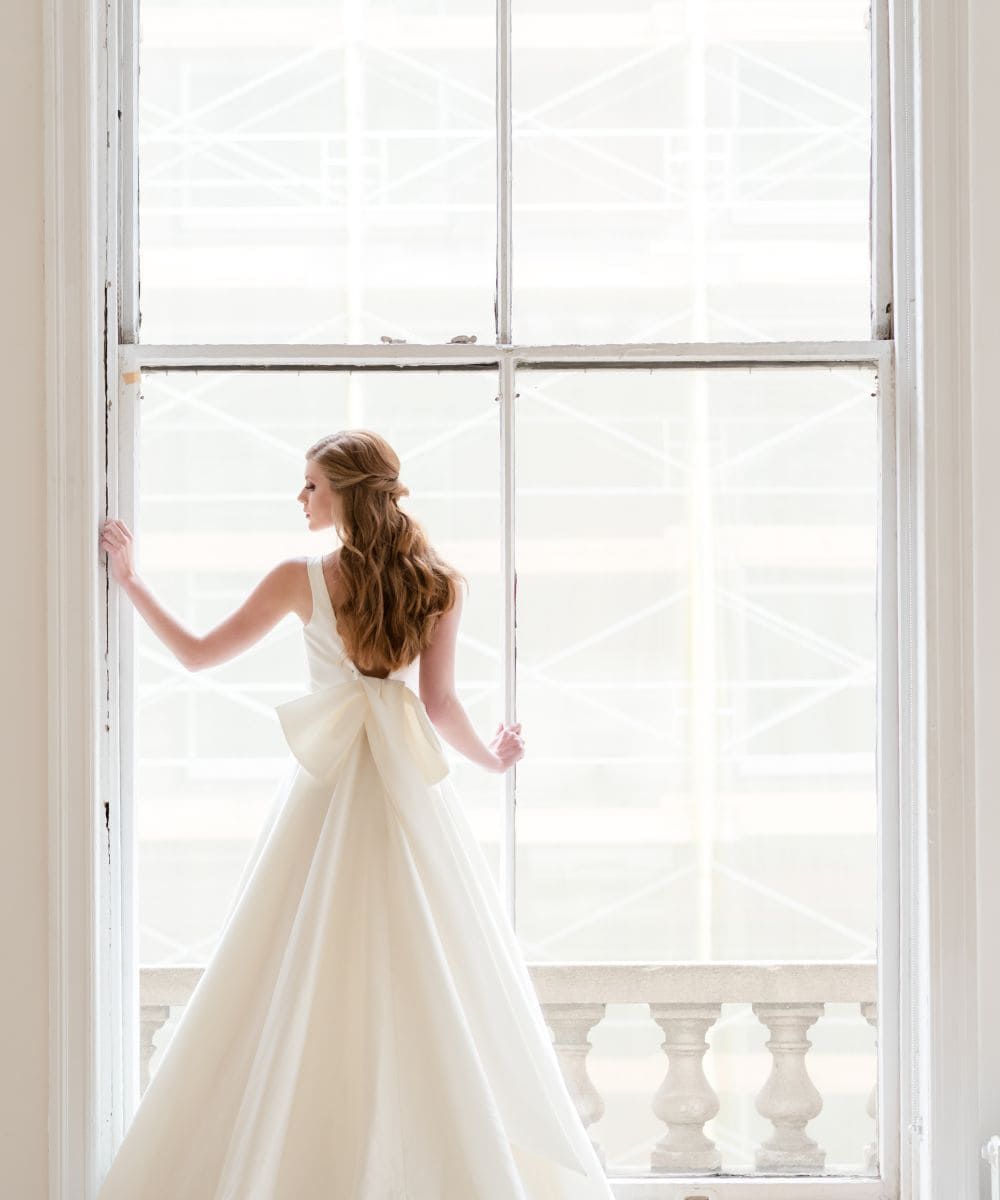 Bride posing by a large window with the back facing the camera