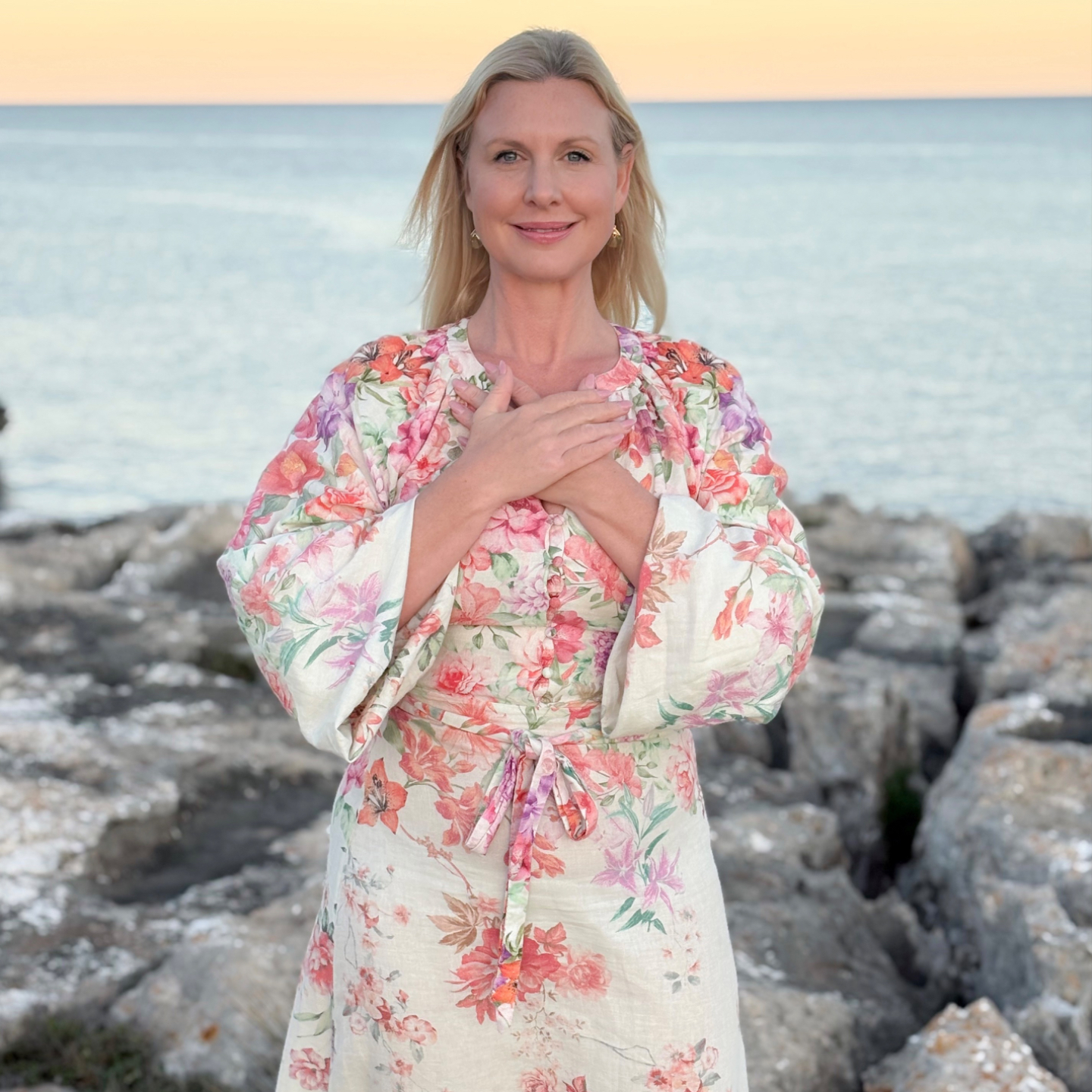 Sofia standing by the water in sunset, leaning her head back, closing her eyes and smiling. 