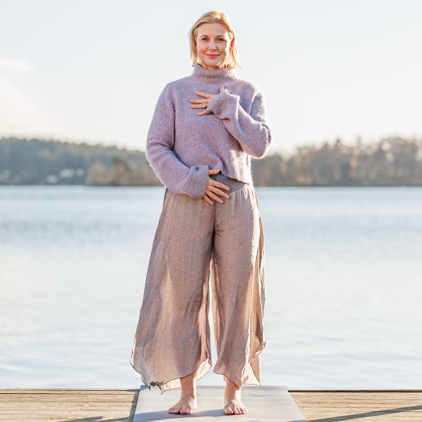 Kvinna står med ryggen mot oss, ser ut över en äng och havet längre bort.