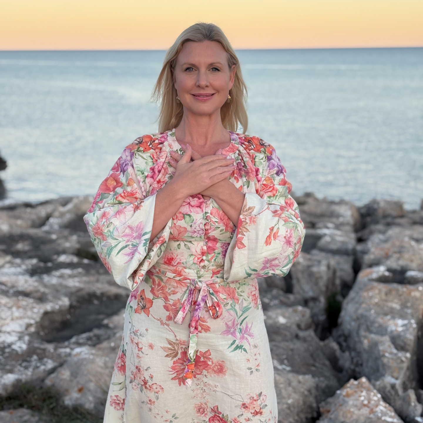 Sofia standing by the water in sunset, leaning her head back, closing her eyes and smiling. 
