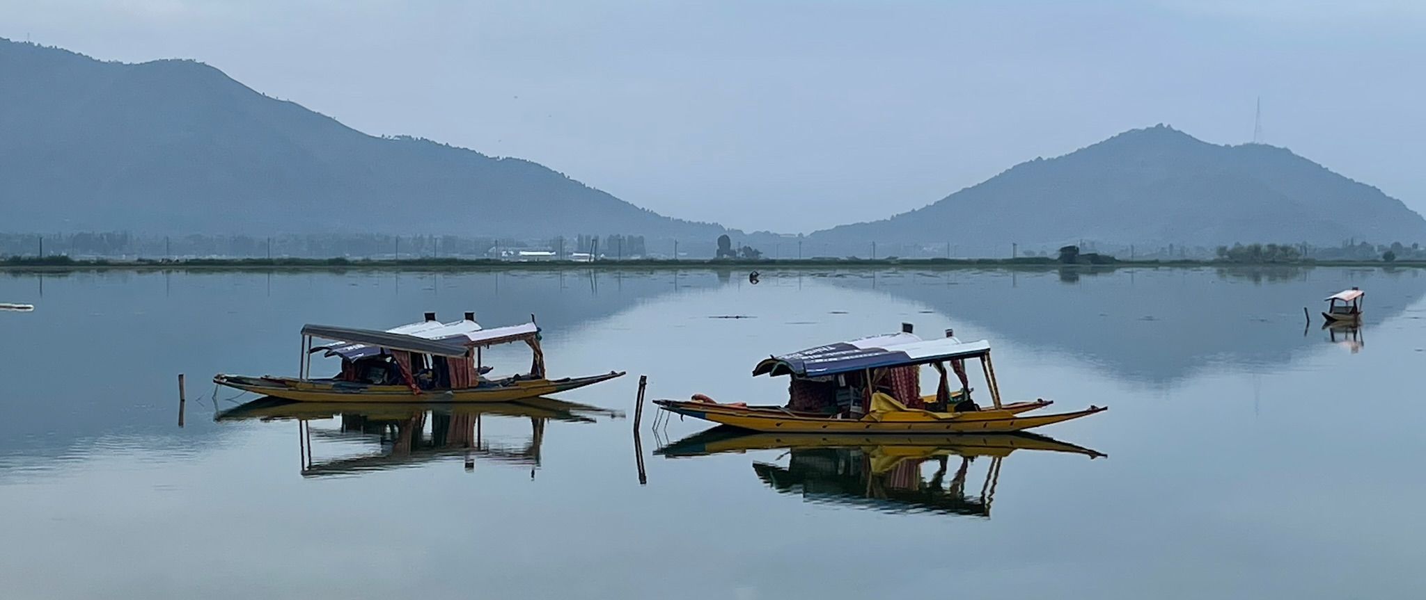 picture of dhal lake with shikaras all in blue gray reflecting the hills behind