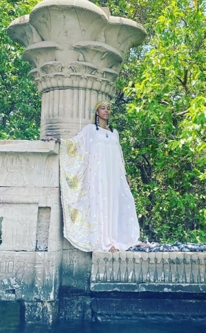 Siri Rishi dressed in white priestess style dress on beach with blue sea in the background upstate New York