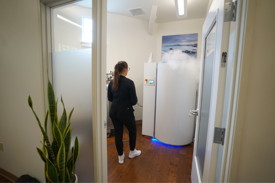 A female employee standing next to a Cryo chamber in a private room. The image showcases the innovative Cryotherapy treatment offered by Evergreen Factor. The employee is seen with a confident and welcoming demeanor, inviting individuals to book their one-time service and discover the transformative power of Evergreen Factor. The private room creates a serene and comfortable atmosphere, enhancing the overall experience. This image represents the commitment of Evergreen Factor to help individuals achieve optimal health and wellness through their innovative treatments. It conveys the message that by choosing Evergreen Factor, individuals can embark on a journey to a healthier and happier self.