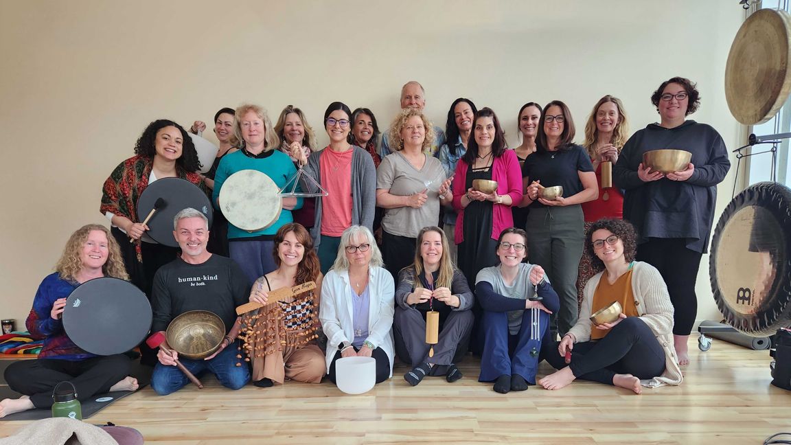 Sound Healing practitioner playing a frame drum with clients lying on mats