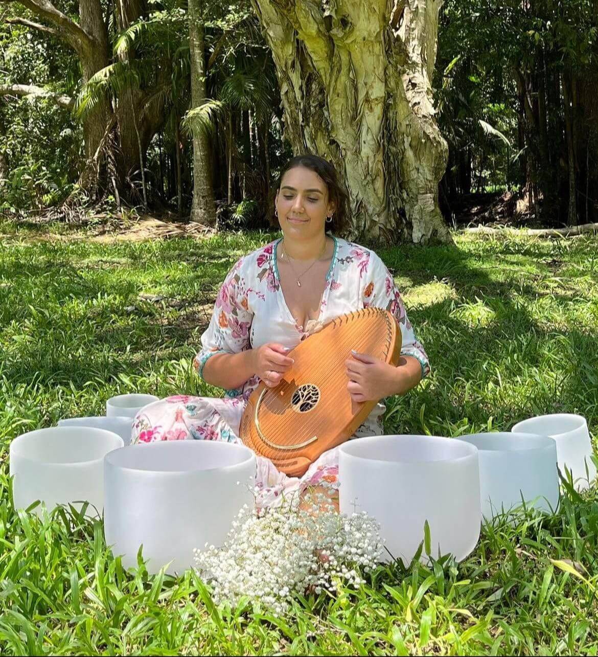 Woman playing a lyre surrounded by crystal singing bowls during an outdoor sound healing meditation