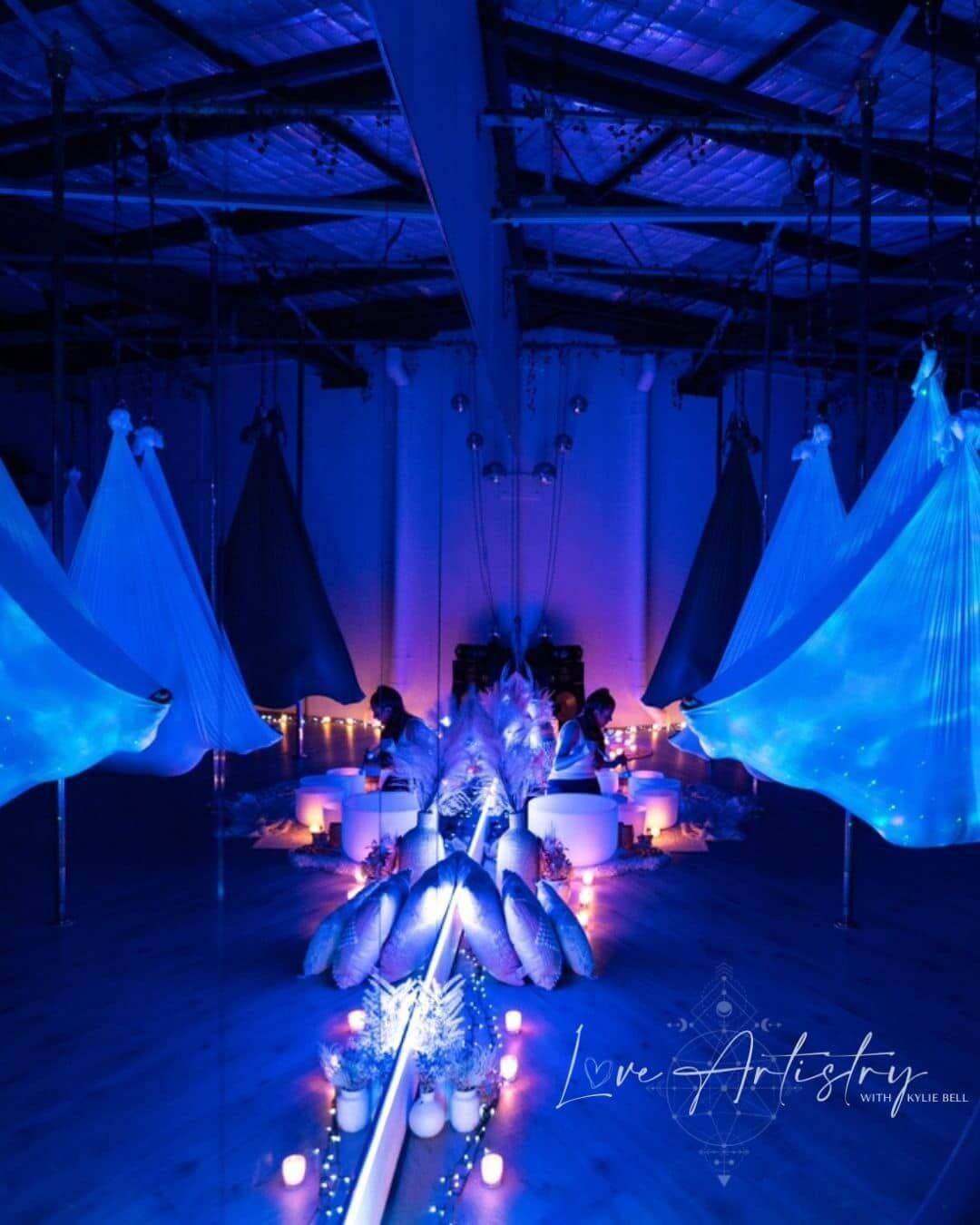 Aerial yoga and sound healing studio with crystal singing bowls, meditation cushions, suspended hammocks, and a relaxing wellness environment