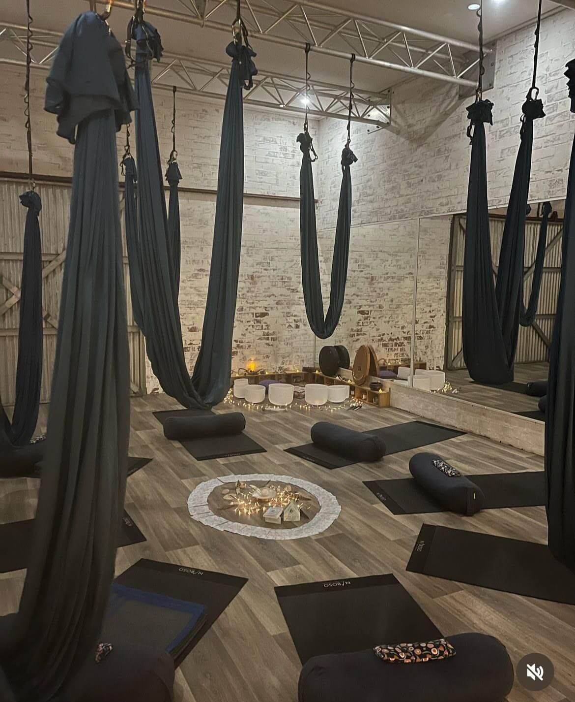 Aerial yoga and sound healing studio with crystal singing bowls, meditation cushions, suspended hammocks, and a relaxing wellness environment