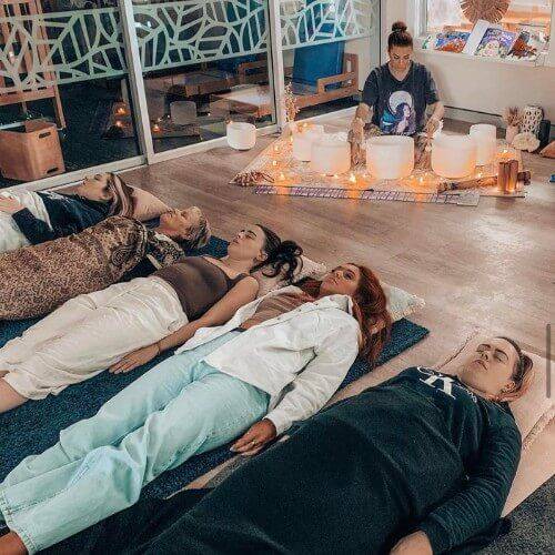 Sound healing session with participants relaxing while a practitioner plays crystal singing bowls.